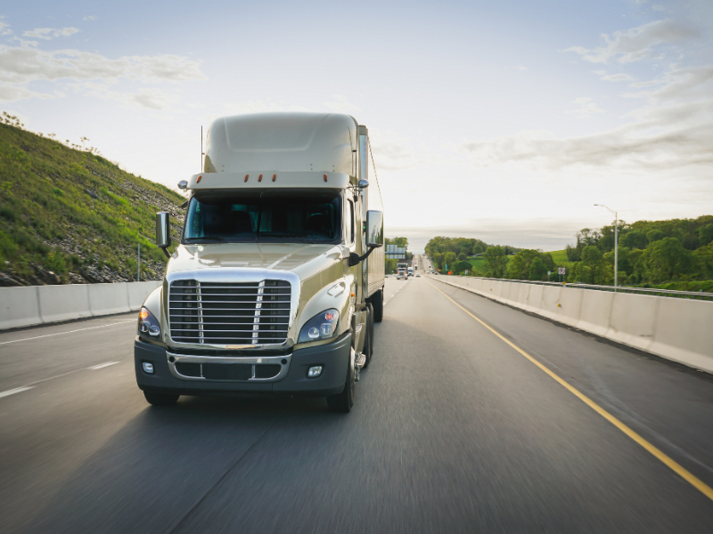 A large truck driving on a highway surrounded by green hills under a blue sky.