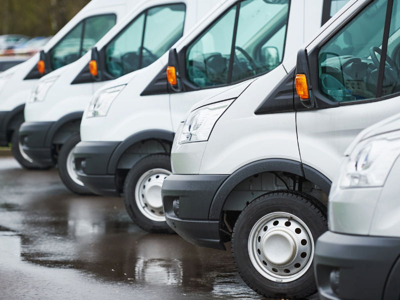 Row of white delivery vans parked on a wet surface, showcasing their front and side views.