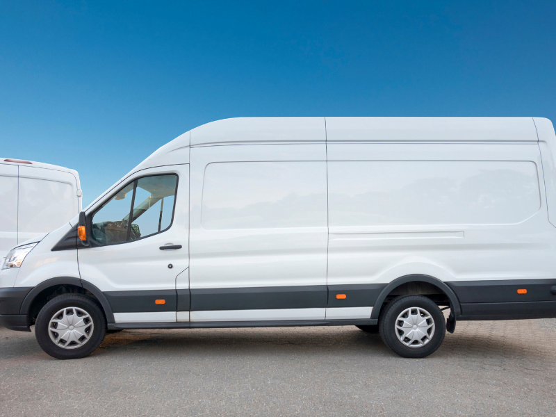 White delivery van parked on asphalt under a clear blue sky.